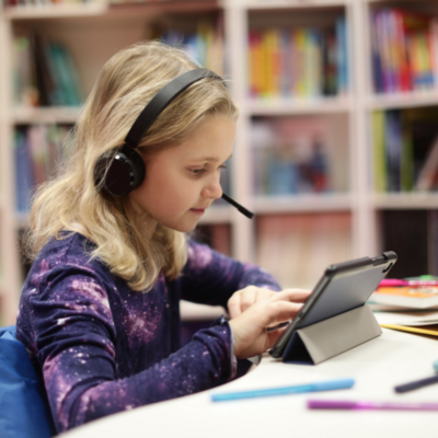 Studentin sitzt mit Headset und Tablet in der Junior Uni-Bibliothek. 