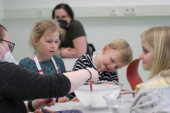 Kinder im Kurs "Zaubereien aus dem Kühlschrank" beugen sich über eine Schüssel mit Flüssigkeit, die von der Dozentin gerührt wird.