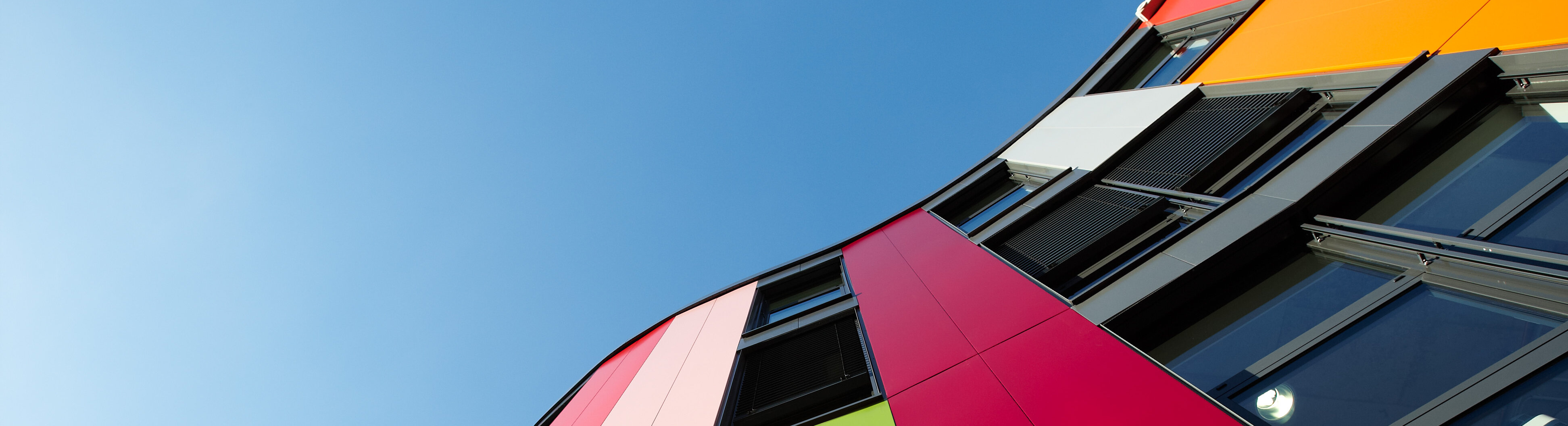 Das bunte Gebäude der Junior Uni aus der Froschperspektive mit klarem, blauen Himmel.