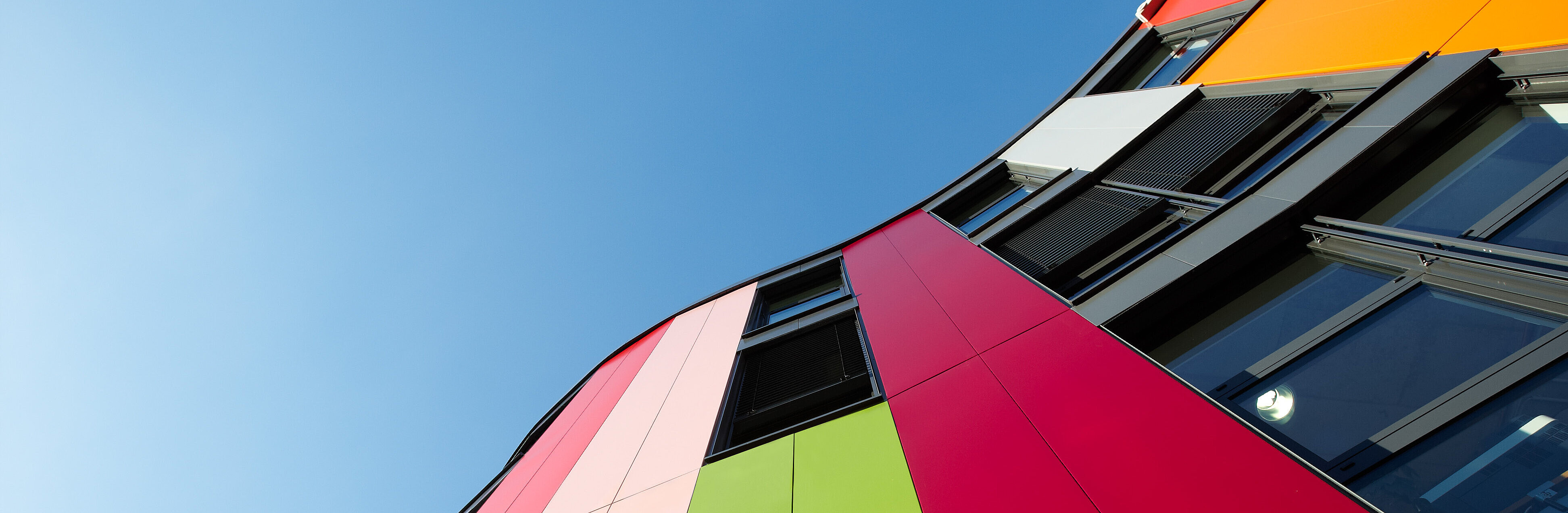 Blick an der bunten Junior Uni-Fassade entlang in den Himmel. 