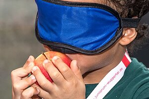 Kind probiert einen Apfel, während es eine Augenbinde trägt