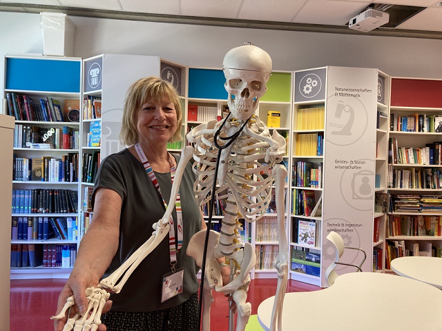Kursbegleiterin Gundi Deister posiert mit dem Junior Uni-Skelett in der Bibliothek. 